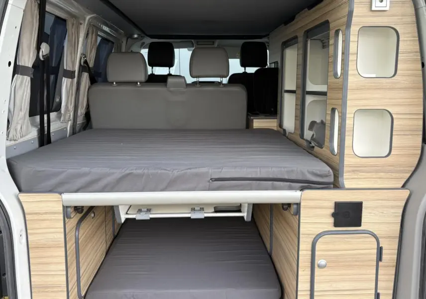 Vue arrière intérieure du Volkswagen Transporter aménagé avec lits superposés et mobilier bois clair.