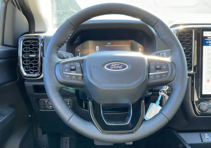 Vue rapprochée du volant en cuir noir du Ford Ranger 2025 gris iconic, avec commandes intégrées et tableau de bord digital.
