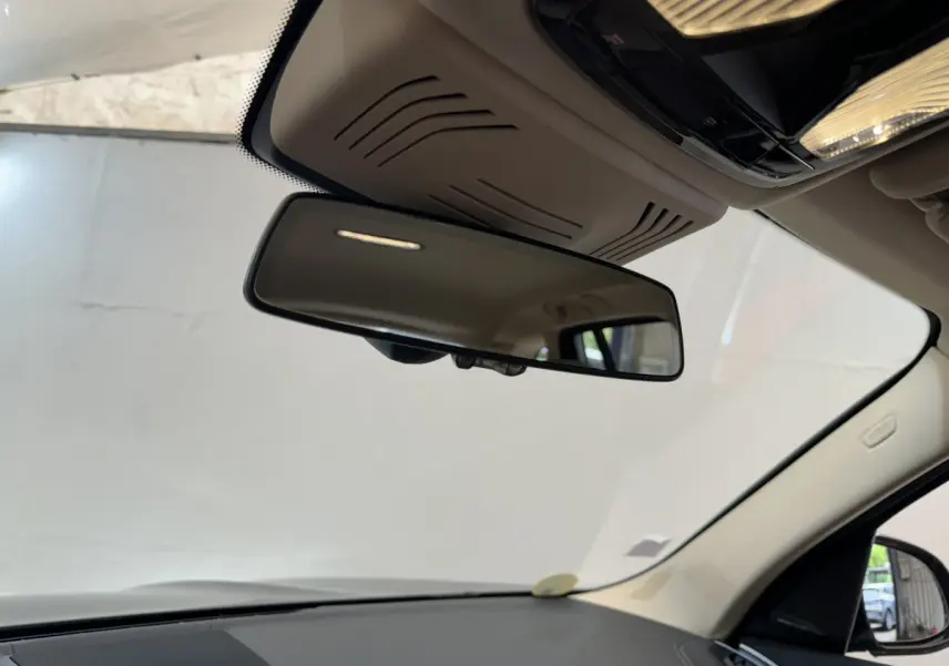 Vue intérieure centrée sur le rétroviseur intérieur d’un BMW X3 gris foncé, avec plafond beige et pare-brise visible.