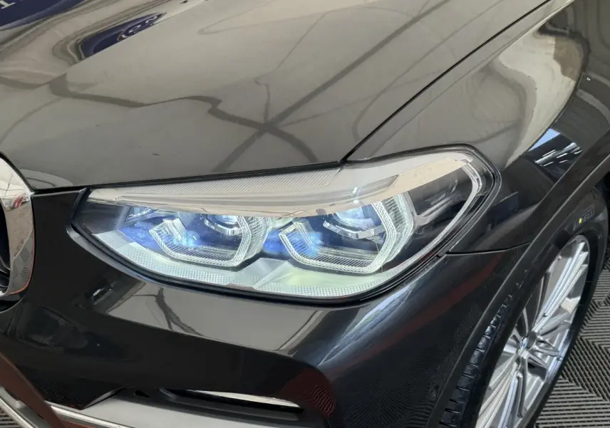 Gros plan sur le phare avant droit LED d’un BMW X3 gris foncé, avec partie de la calandre et jante visible.