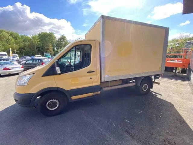 Vue de profil côté gauche d'un fourgon Ford Transit jaune avec caisse 12m3 et hayon arrière sous un ciel partiellement nuageux.