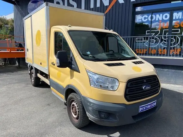 Vue 3/4 avant droite d'un Ford Transit Chassis Cabine jaune avec caisse 12m3 et hayon, stationné devant un bâtiment.