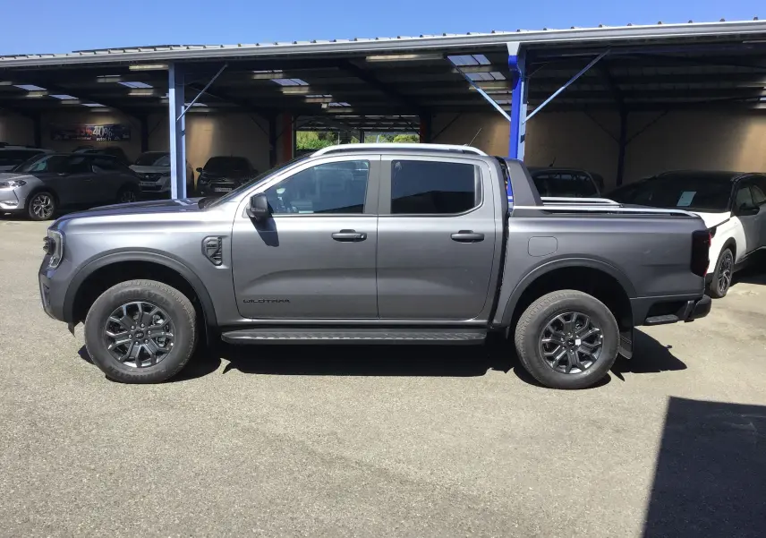 Ford Ranger Double Cabine Wildtrak gris carbone vu de profil côté gauche, avec rideau de plateau et marchepied visibles.