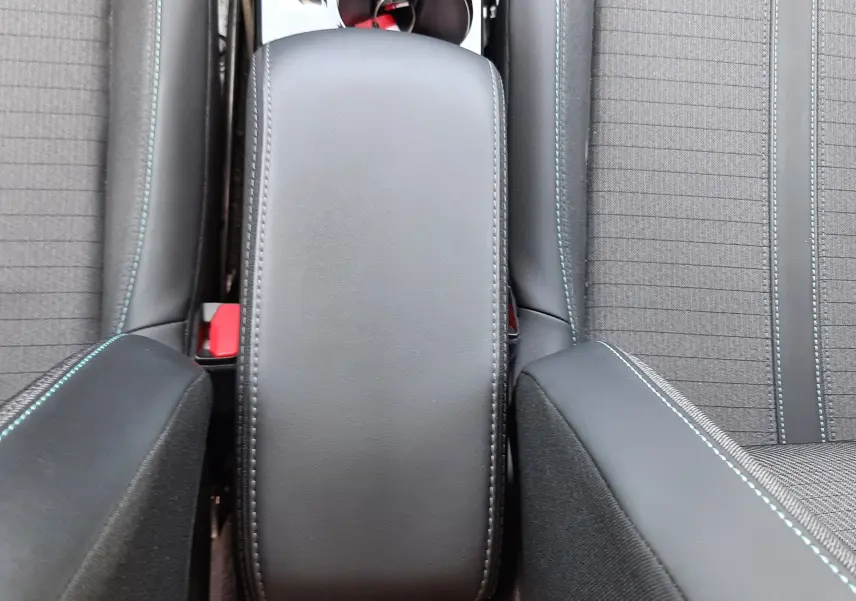 Vue plongeante sur l'accoudoir central noir et les sièges tissu gris avec surpiqûres bleues d'un Peugeot 2008 2022