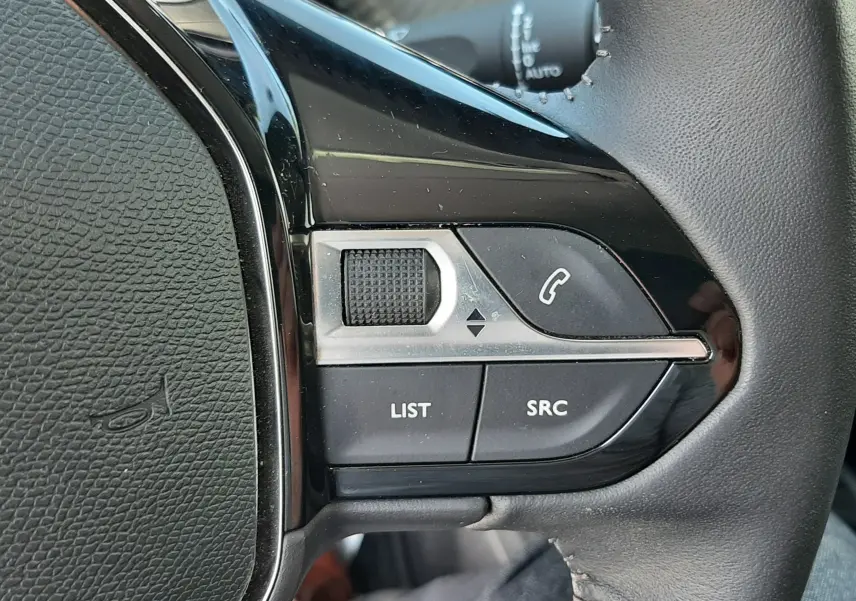 Gros plan sur les commandes gauche du volant noir d'un Peugeot 2008 gris Artense, boutons de téléphone et liste visibles.