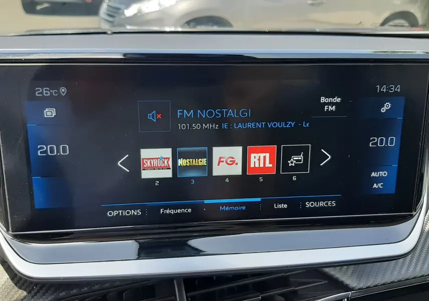 Écran tactile central du Peugeot 2008 gris Artense affichant les stations radio FM avec commandes climatisation à 20°C.