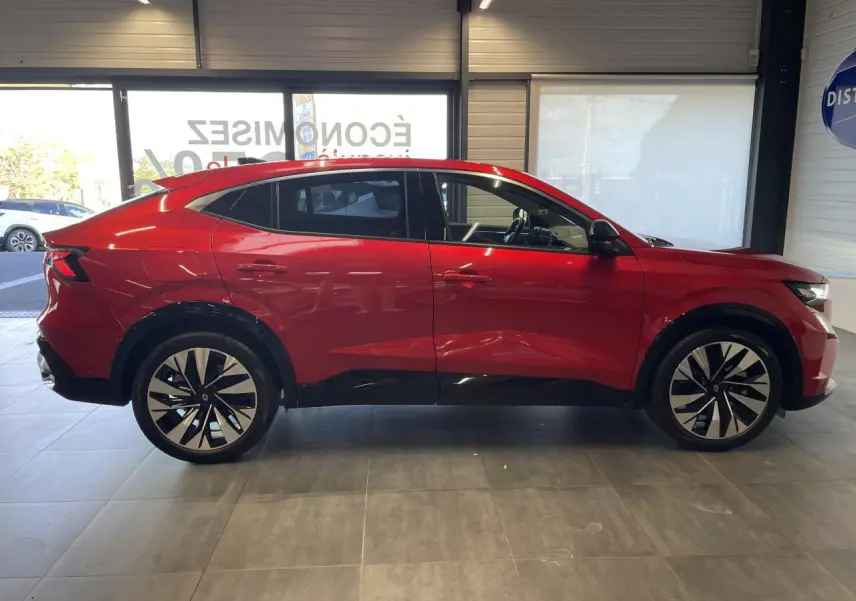 Profil droit du Renault Rafale rouge avec toit noir, jantes alliage bicolores et lignes dynamiques en intérieur showroom.