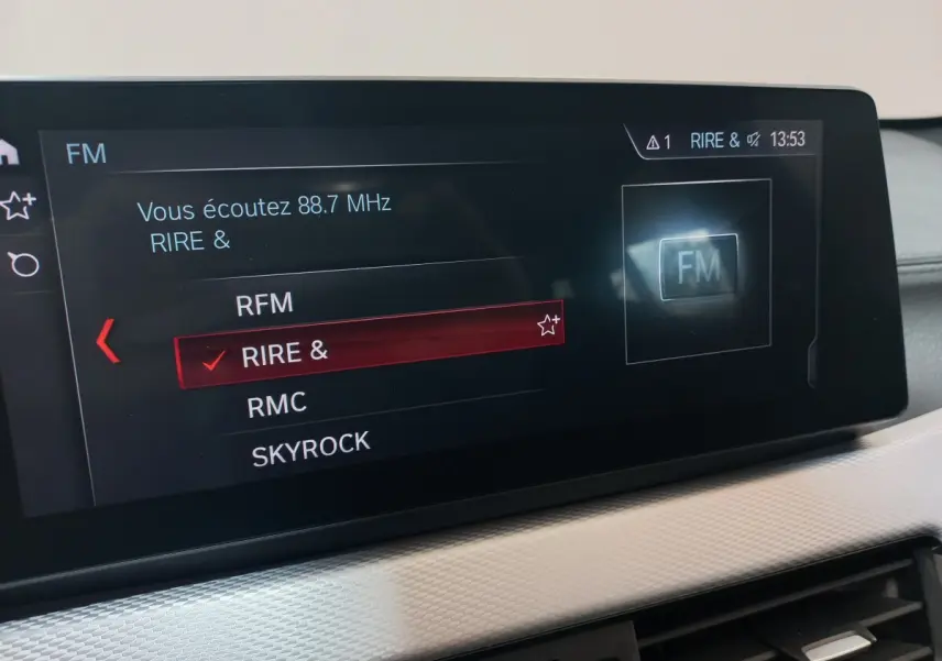 Écran tactile central affichant la sélection radio FM dans l’habitacle d’un BMW X1 noir, vue intérieure rapprochée.