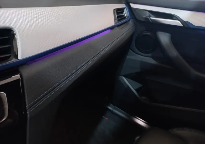 Intérieur avant droit de BMW X1 xDrive20d 2022, tableau de bord noir et beige avec éclairage d'ambiance violet.