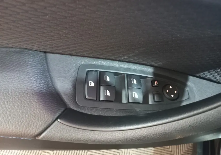 Gros plan sur les commandes des vitres électriques côté conducteur d’un BMW X1 noir, intérieur cuir noir.