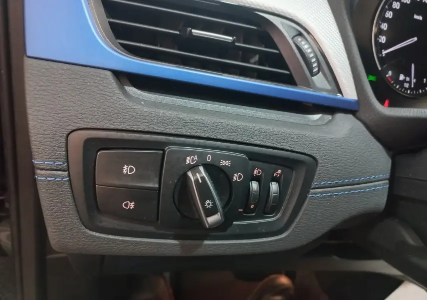 Détail du tableau de bord noir et bleu du BMW X1 2022, avec commandes d’éclairage et ventilation visibles.