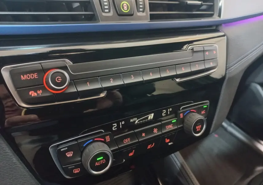 Gros plan sur la console centrale noire du BMW X1 xDrive20d M Sport 2022 avec commandes climatisation digitale et boutons lumineux.