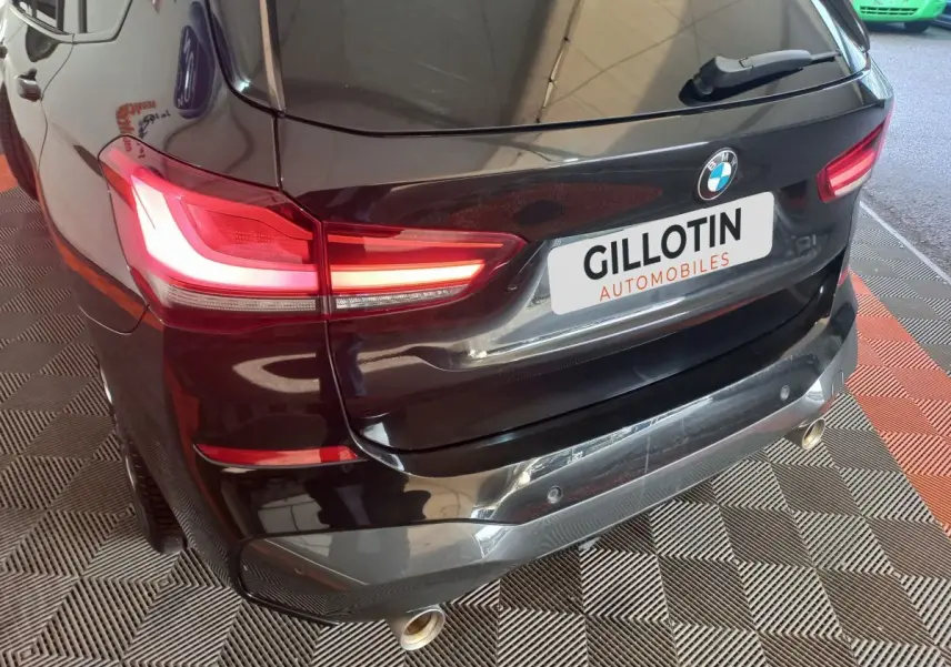 Vue 3/4 arrière droite d’un BMW X1 xDrive20d M Sport noir avec feux LED allumés et double sortie d’échappement chromée.