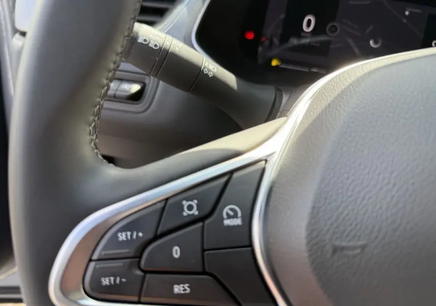 Gros plan sur les commandes au volant du Renault Captur 2025, avec boutons de régulateur et tableau de bord numérique en arrière-plan.