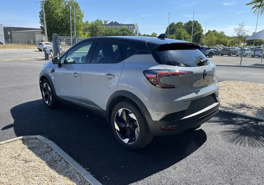 Renault Captur 2025 gris rafale avec toit noir, vu en 3/4 avant droit devant un bâtiment industriel.