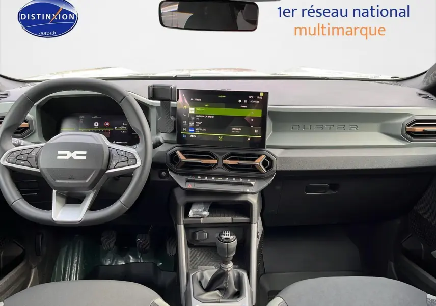 Vue intérieure avant du tableau de bord du Dacia Duster 2025 avec volant multifonction et écran tactile central.