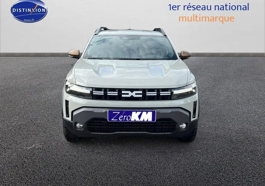 Vue frontale du Dacia Duster 2025 couleur Sandstone avec calandre noire et plaques Zero KM visibles.