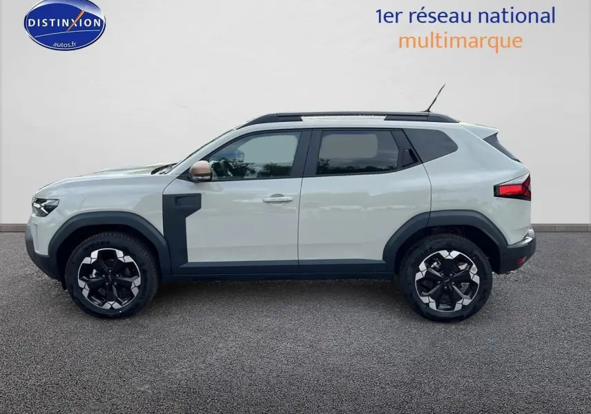 Vue de profil côté gauche du Dacia Duster 2025 Sandstone avec barres de toit et jantes 18 pouces noires et argentées.