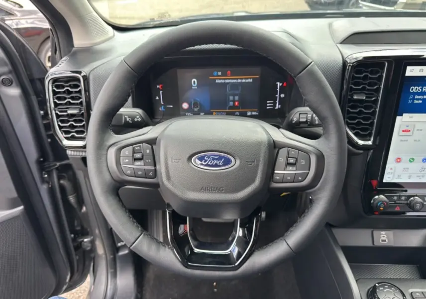 Vue centrée du volant noir du Ford Ranger 2025 gris carbone, avec tableau de bord digital et écran tactile visible.