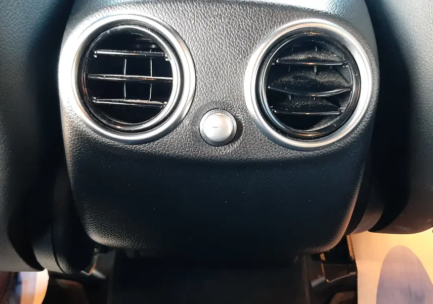 Gros plan sur les aérateurs arrière ronds chromés de l'habitacle noir du Mercedes GLC Coupé 300 AMG Line blanc.