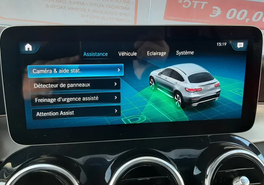 Écran central montrant l'assistance caméra et aide au stationnement d'un Mercedes GLC Coupé blanc en vue arrière 3/4.