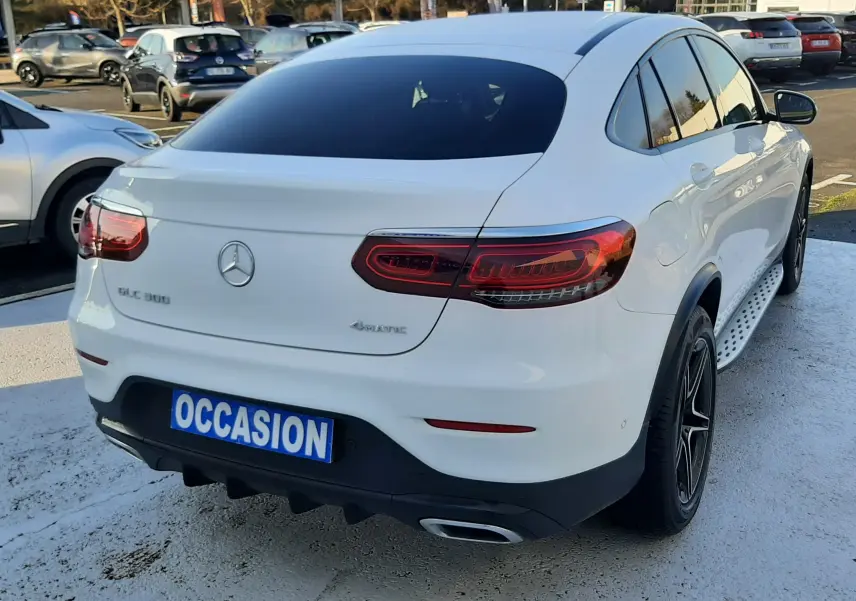 Vue 3/4 arrière droite d'un Mercedes GLC Coupé blanc avec feux LED et jantes noires sur parking.