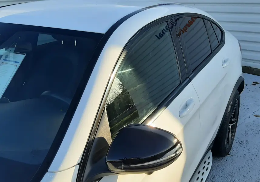 Vue 3/4 avant droit d'un Mercedes GLC Coupé blanc avec rétroviseur noir et jantes AMG noires.