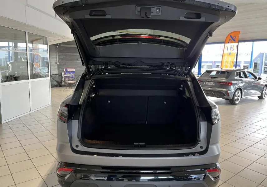 Vue arrière d’un Renault Austral gris avec hayon motorisé ouvert montrant le coffre spacieux en intérieur showroom.