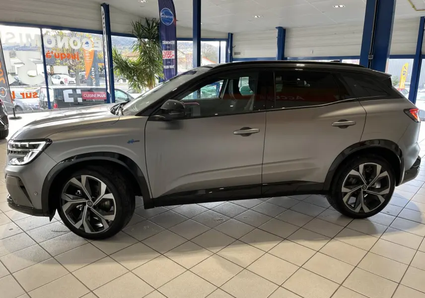 Vue latérale droite du Renault Austral gris avec toit noir étoilé et jantes alliage 20 pouces dans un showroom.