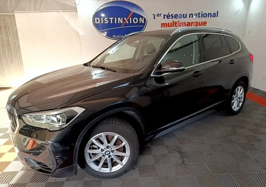 BMW X1 sDrive20i noir vue 3/4 avant droit en intérieur avec jantes alliage et phares LED allumés
