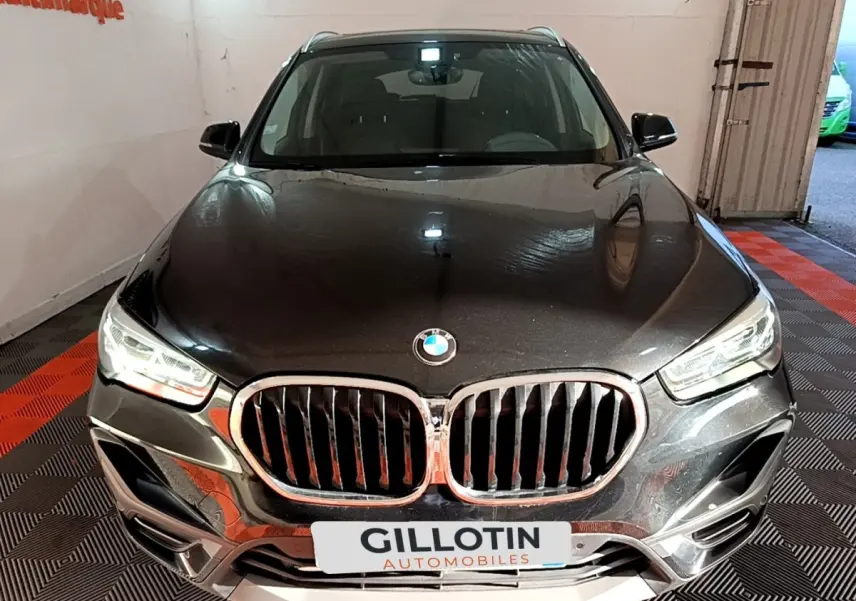 Vue frontale d'un BMW X1 sDrive20i noir avec calandre chromée et phares LED allumés en intérieur showroom.