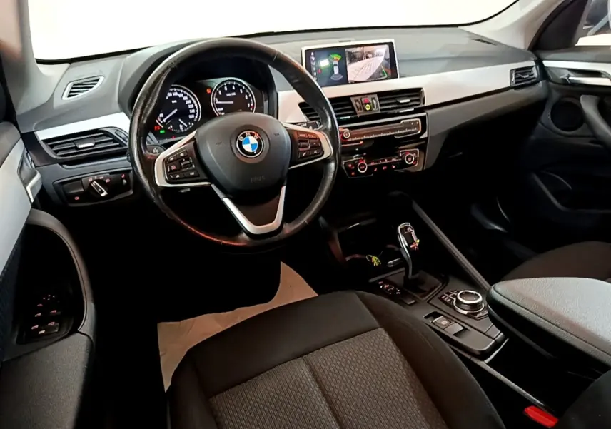 Vue intérieure côté conducteur du BMW X1 2020 noir, avec volant cuir multifonctions et écran tactile 8,8 pouces allumé.