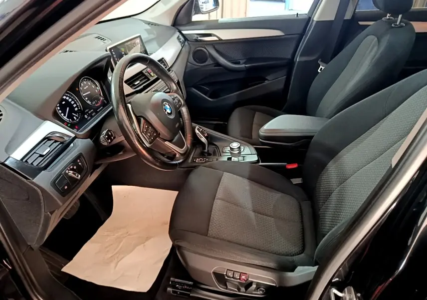 Vue intérieure côté conducteur d’un BMW X1 noir, montrant le volant cuir multifonctions et la console centrale avec écran tactile.