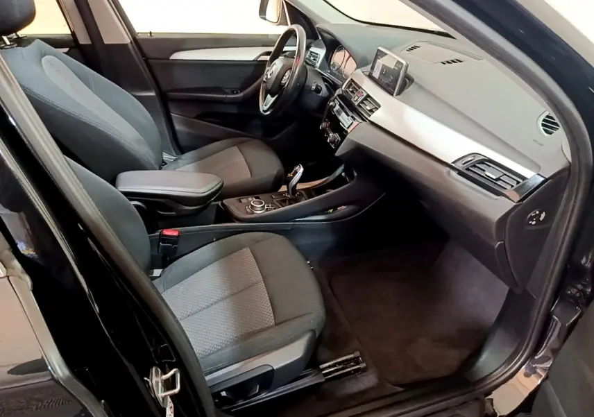 Intérieur côté conducteur d’un BMW X1 noir 2020, montrant sièges tissu gris et tableau de bord avec écran tactile.