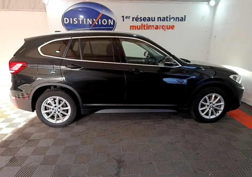 BMW X1 sDrive20i noir vue de profil côté gauche dans un showroom avec logo Distinxion en arrière-plan.
