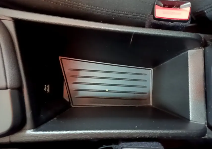 Gros plan sur le rangement central noir du BMW X1 sDrive20i, avec bouton de sécurité rouge visible en haut à droite.