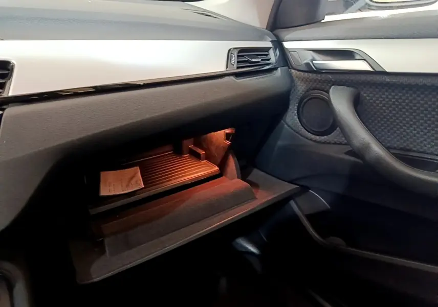 Intérieur BMW X1 2020, vue côté passager sur boîte à gants ouverte avec éclairage orange et garnitures noires et grises.