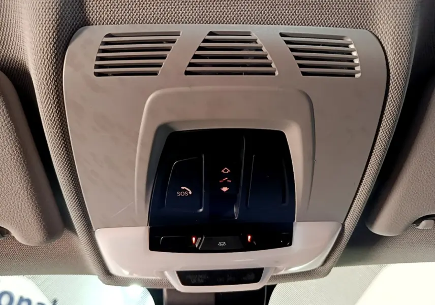 Vue en contre-plongée du plafonnier gris clair avec commandes SOS et éclairage intérieur d'une BMW X1 noire de 2020.