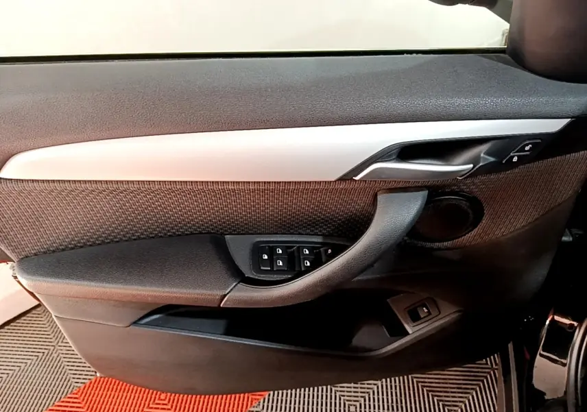 Vue intérieure côté gauche de la porte avant d'une BMW X1 noire, avec commandes de vitres et poignée intégrée.