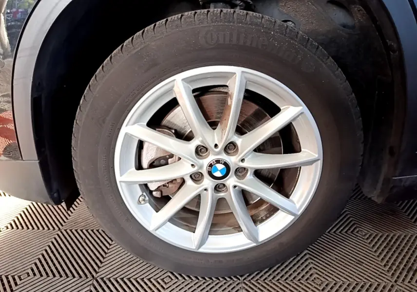 Gros plan sur la roue avant gauche d’un BMW X1 noir, mettant en valeur la jante argentée à 10 branches.