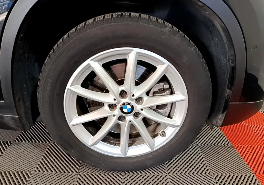 Gros plan sur la roue avant droite d’un BMW X1 noir, mettant en valeur la jante alliage argentée à 10 branches.