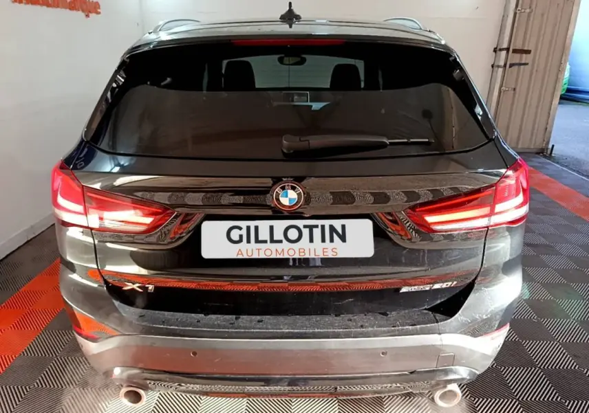 Vue arrière d’un BMW X1 sDrive20i noir avec feux LED allumés et double sortie d’échappement visible.