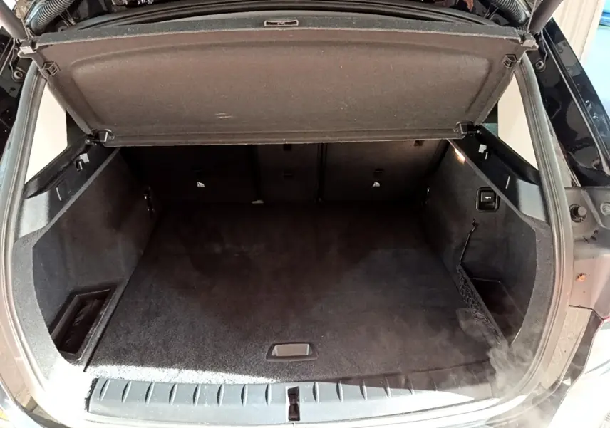 Coffre ouvert vu de l'arrière d'un BMW X1 noir, montrant un espace de rangement propre et bien agencé.