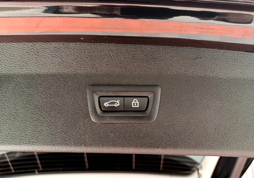 Boutons de fermeture et verrouillage électrique du coffre sur le hayon d’un BMW X1 noir, vue intérieure rapprochée.