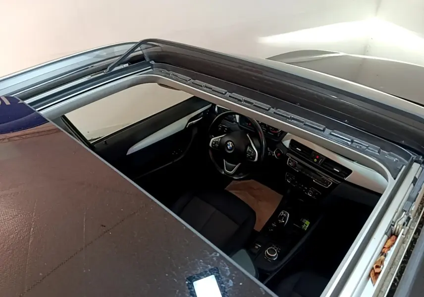 Vue plongeante sur l'intérieur noir d'une BMW X1 sDrive20i 2020 avec toit ouvrant panoramique partiellement ouvert.