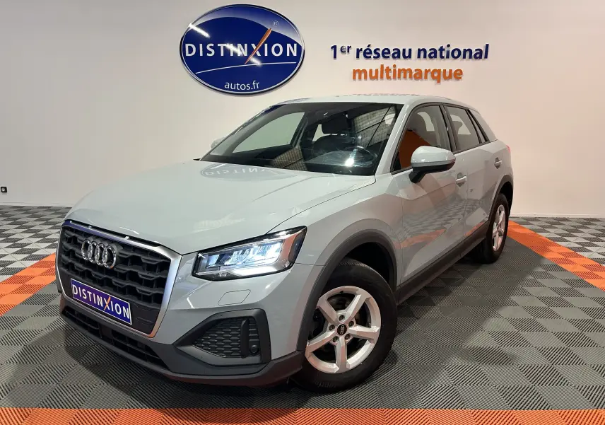 Audi Q2 gris en 3/4 avant droit, phares allumés, sur sol damier avec logo Distinxion en arrière-plan.