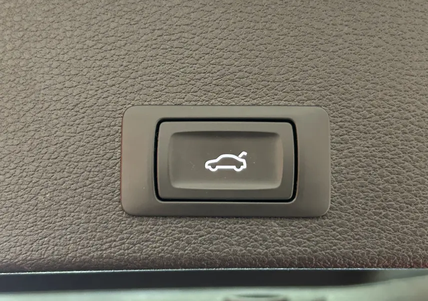 Bouton noir de hayon électrique avec icône blanche sur panneau en cuir marron dans un Audi Q2 gris 2023.