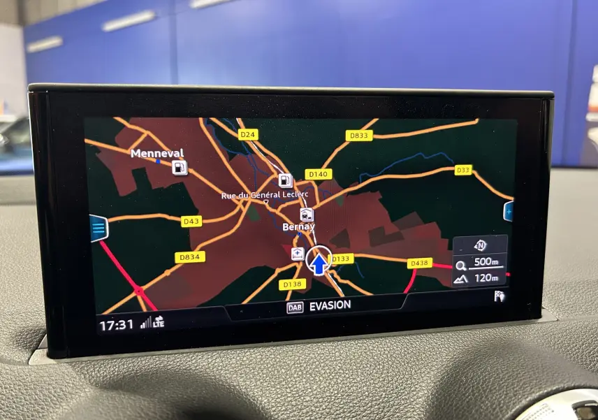 Écran GPS en gros plan à l’intérieur d’un Audi Q2 gris, affichant une carte routière avec navigation active.