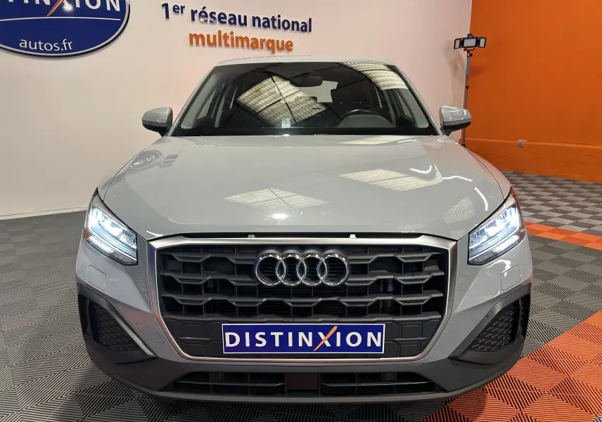 Vue frontale d'un Audi Q2 gris avec calandre noire et phares LED allumés dans un showroom.