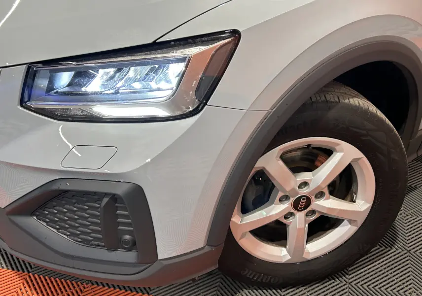 Gros plan sur l'avant droit gris d'un Audi Q2 2023, mettant en valeur le phare LED et la jante alliage cinq branches.